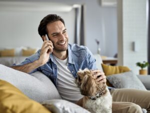 Happy man talking on cell phone while relaxing with a dog at home.